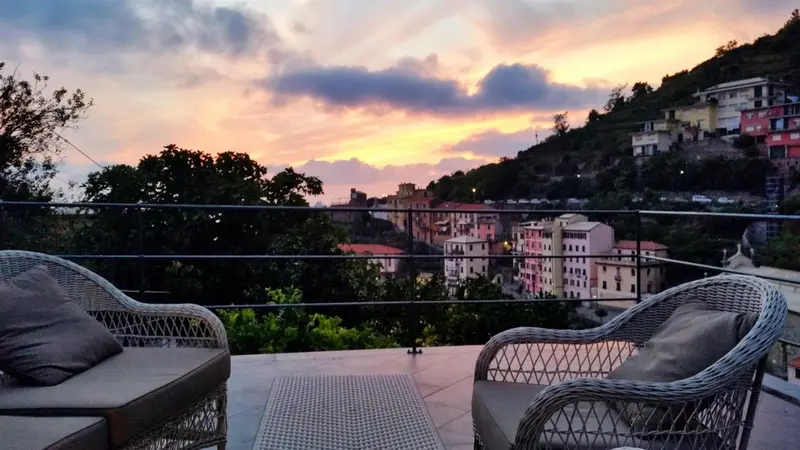 Deux fauteuils en osier invitent à la détente sur une terrasse avec vue sur une ville côtière au coucher du soleil.