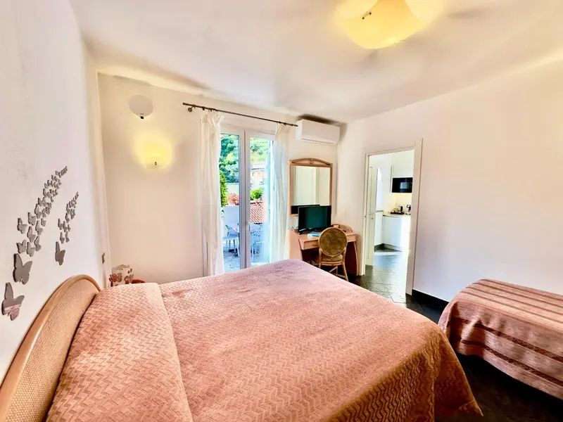 Une chambre lumineuse avec un lit recouvert d'une courtepointe rose et un bureau près d'une porte-fenêtre.