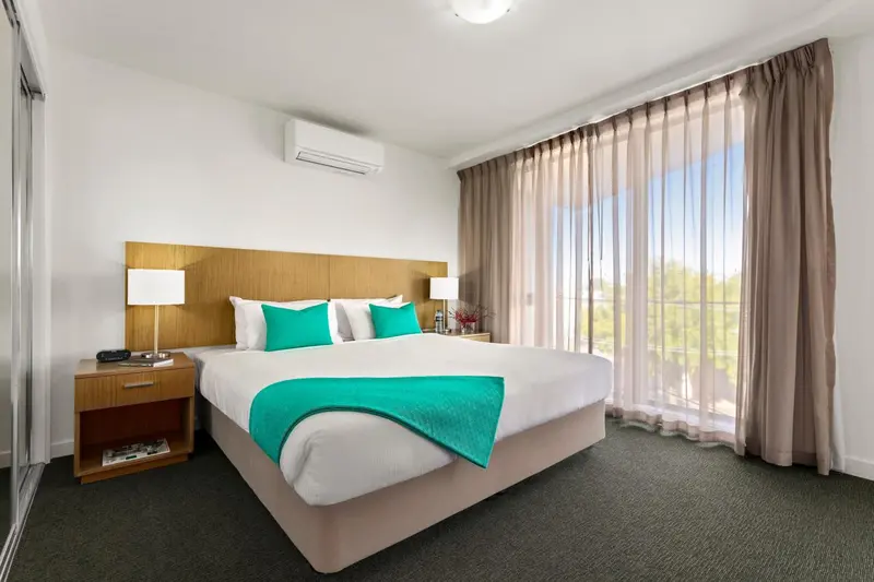 Une chambre lumineuse avec un grand lit recouvert d'une courtepointe turquoise.