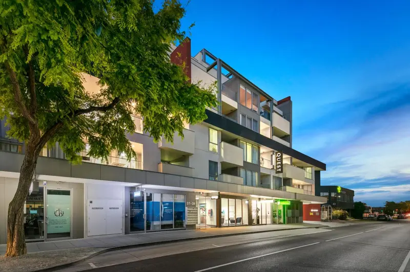 Bâtiment moderne avec des balcons et des arbres en premier plan.