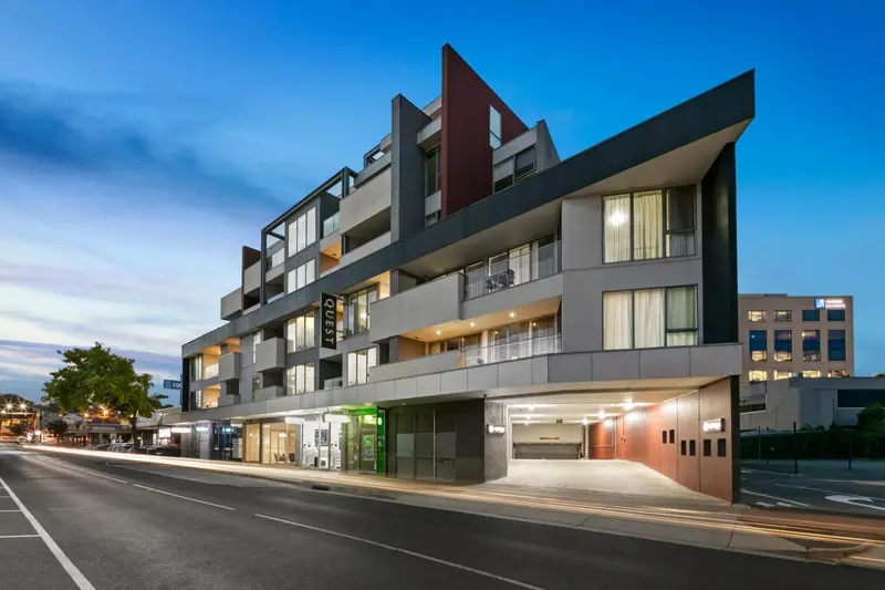 Bâtiment moderne avec des balcons et une entrée illuminée le long d'une rue.