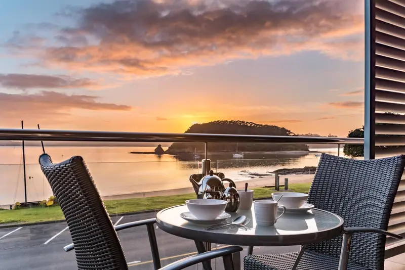 Une table avec une service à thé est placée sur une terrasse avec vue sur la mer au coucher du soleil.