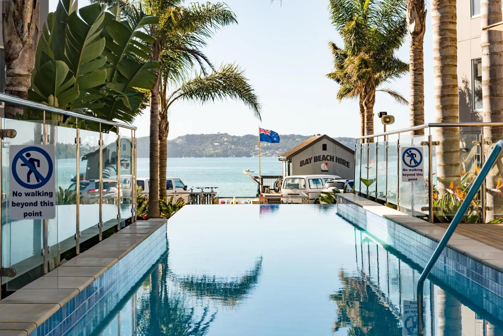 Piscine rectangulaire bleue bordée d'une terrasse ensoleillée avec vue sur la mer.