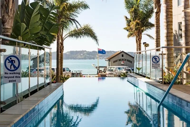 Piscine rectangulaire bleue bordée d'une terrasse ensoleillée avec vue sur la mer.