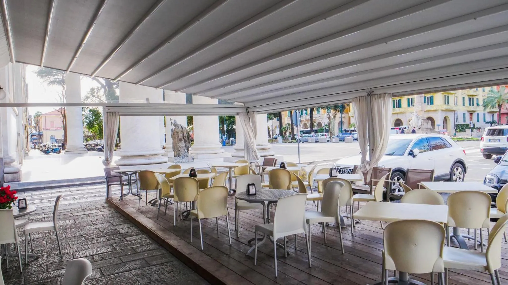 Terrasse ombragée avec tables et chaises en plastique blanc.