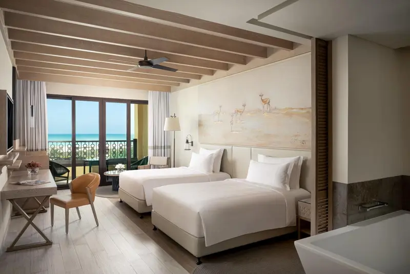 Chambre lumineuse avec deux lits simples et vue sur la mer.