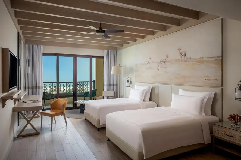 Chambre lumineuse avec deux lits simples et balcon.