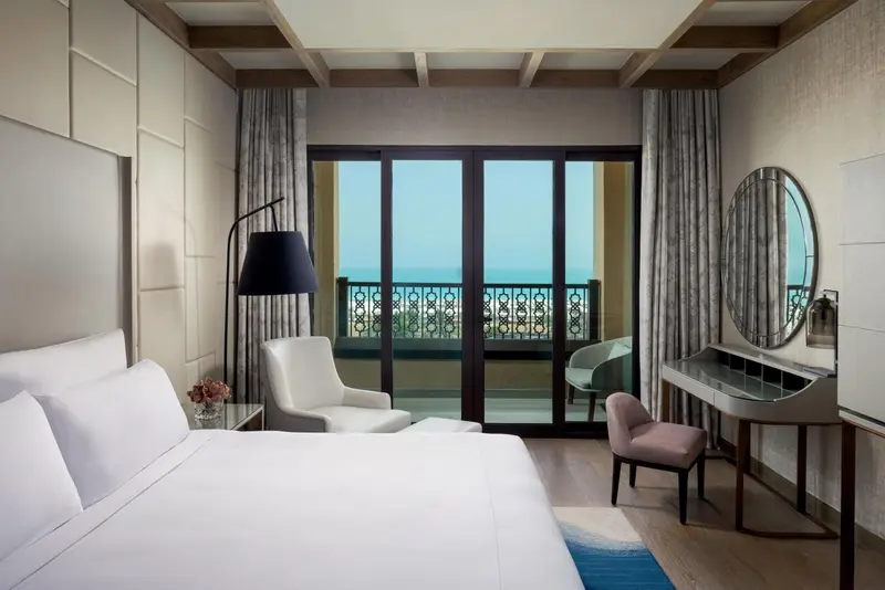 Une chambre lumineuse avec un grand lit et un accès à un balcon donnant sur la mer.