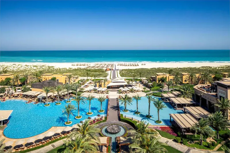 Vue aérienne d'un complexe hôtelier avec piscines et végétation luxuriante face à une plage.