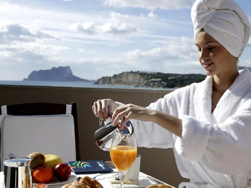 Une femme verse du jus d'orange sur une table de petit-déjeuner en terrasse.