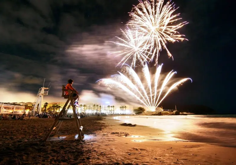 Feux d'artifice illuminant une plage nocturne.