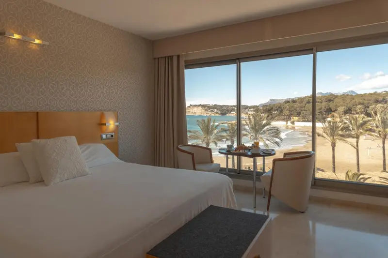Chambre lumineuse avec vue sur la mer et une petite table avec des boissons.