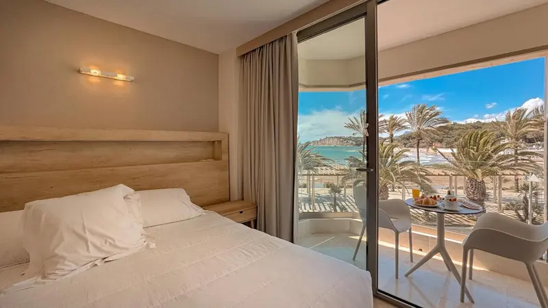 Une chambre lumineuse avec un lit et un balcon donnant sur la mer.
