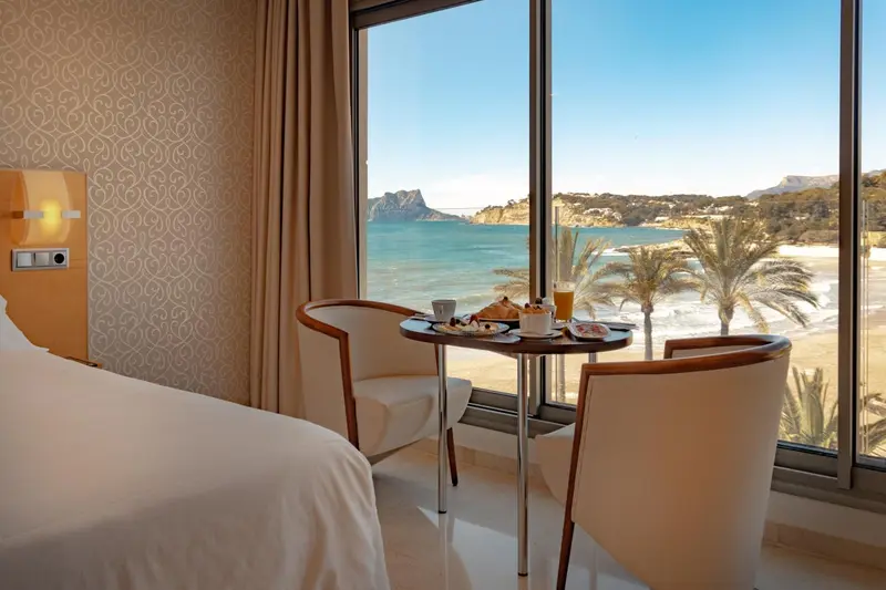 Une table avec un petit-déjeuner est placée devant une grande fenêtre donnant sur la mer et la plage.