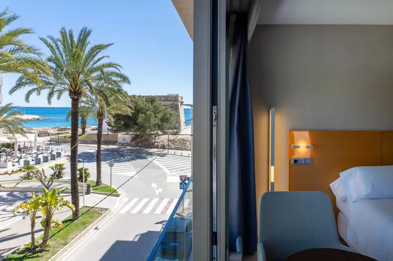 Vue d'une chambre d'hôtel donnant sur la mer et la végétation.