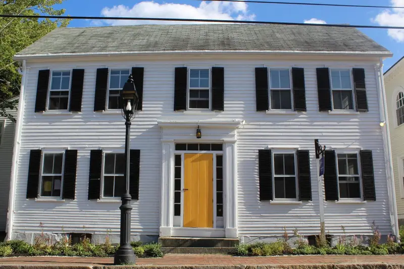 Façade d'une maison blanche à deux étages avec des volets noirs et une porte jaune.