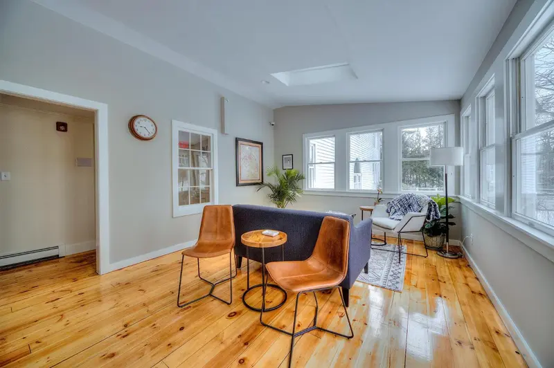 Espace de détente lumineux avec canapés et fauteuils près de grandes fenêtres.