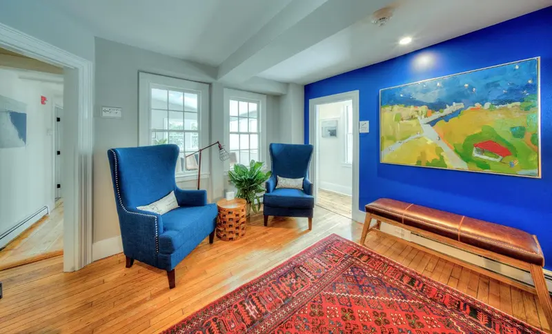 Un salon chaleureux avec deux fauteuils bleus et un tapis oriental.