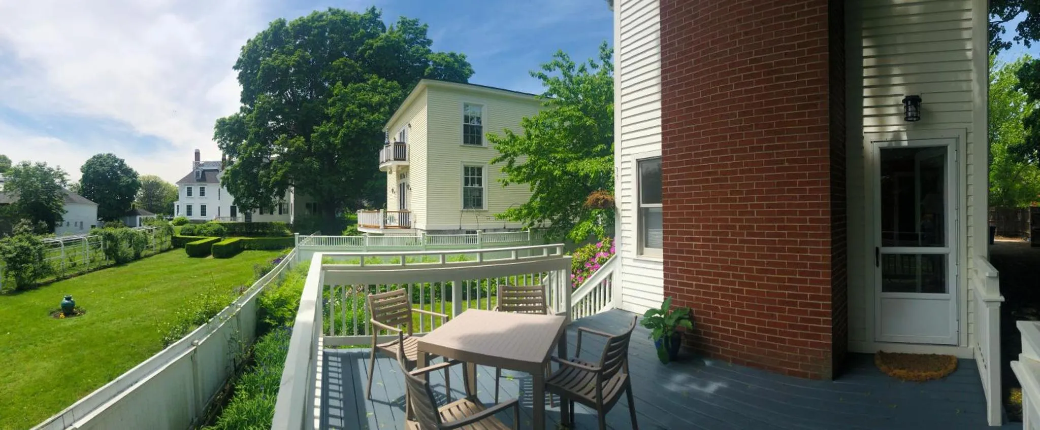 Terrasse avec mobilier de jardin donnant sur une pelouse et des bâtiments.