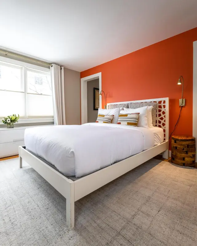 Une chambre lumineuse avec un grand lit blanc et un mur orange.