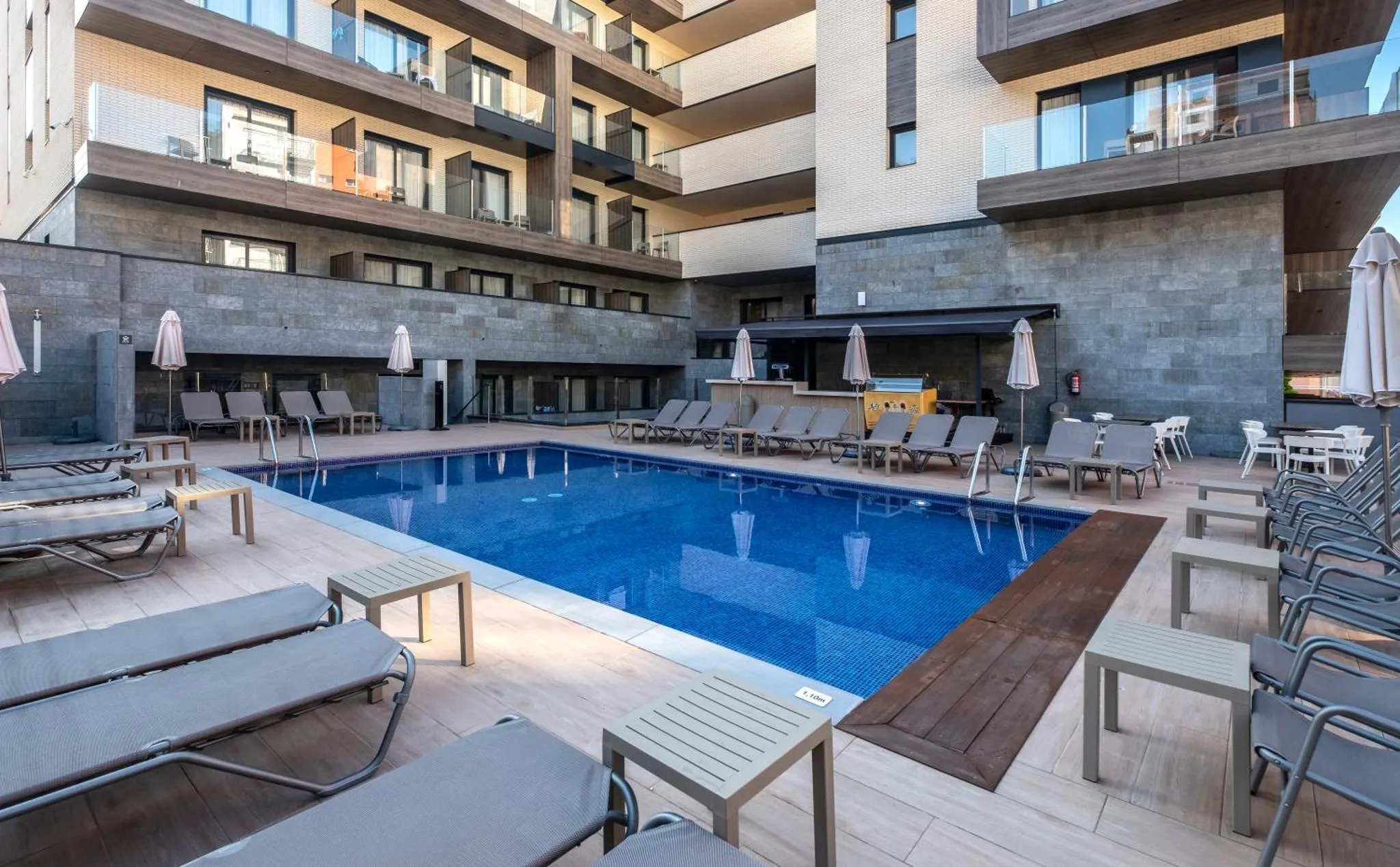 Une piscine rectangulaire avec des transats et des parasols est entourée d'une terrasse.