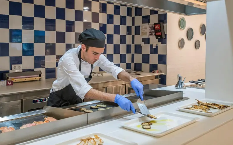 Un chef prépare des plats sur une plaque de cuisson en acier inoxydable.