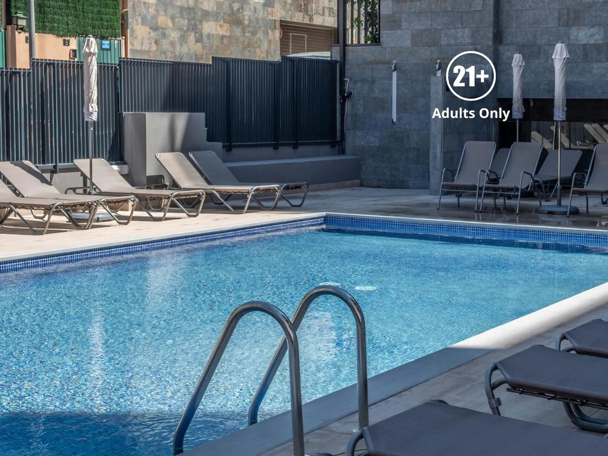 Transats gris disposés autour d'une piscine bleue ensoleillée.