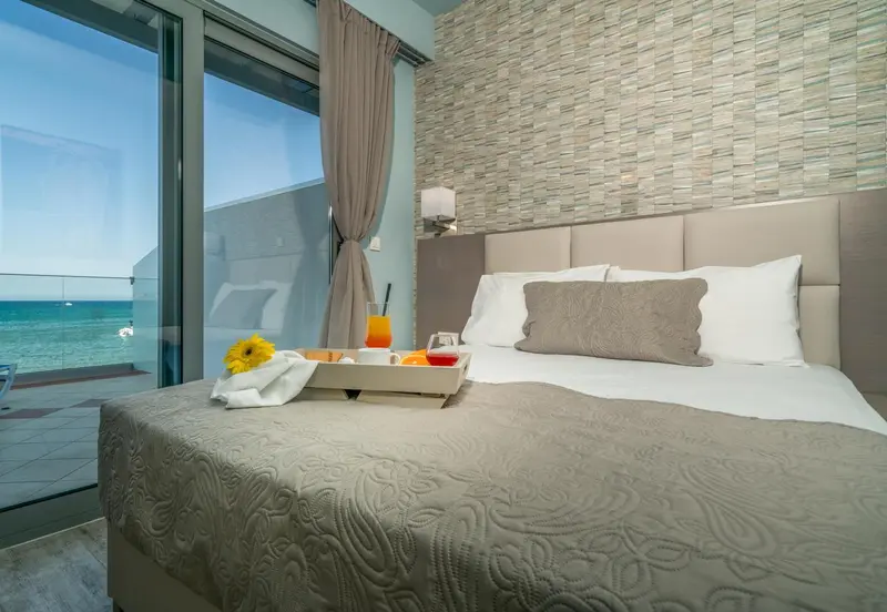 Un lit confortable avec un plateau de petit-déjeuner est placé devant une grande baie vitrée donnant sur la mer.