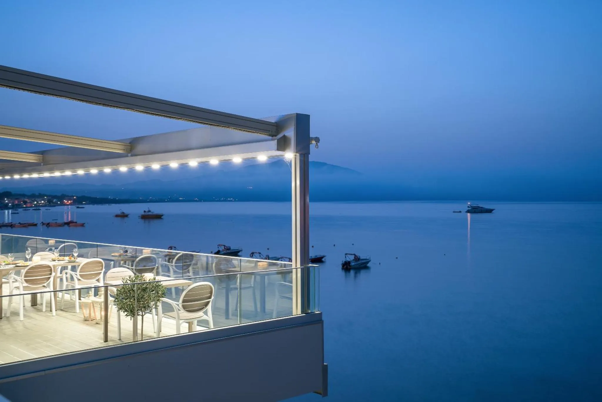 Terrasse lumineuse avec tables et chaises donnant sur la mer au crépuscule.