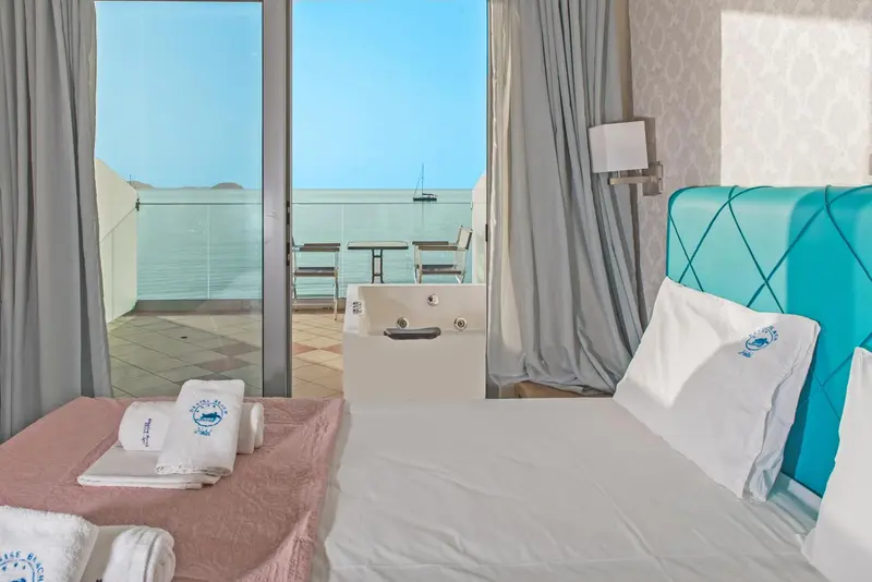Une chambre lumineuse avec un lit turquoise donnant sur une vue mer.