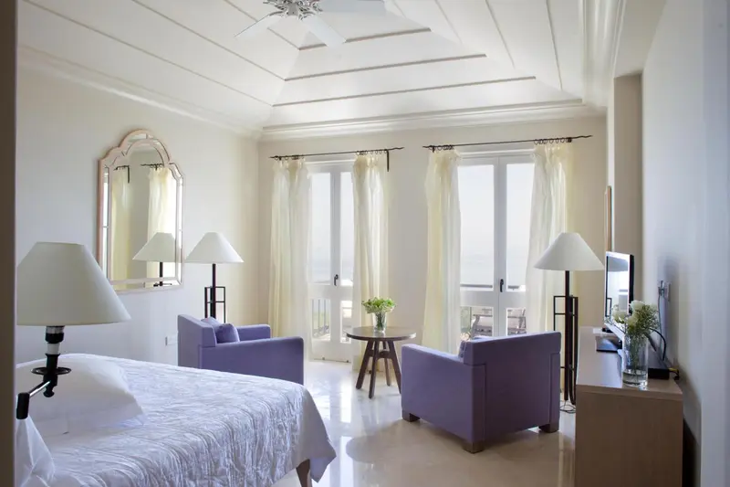 Une chambre lumineuse avec un lit et deux fauteuils violets.