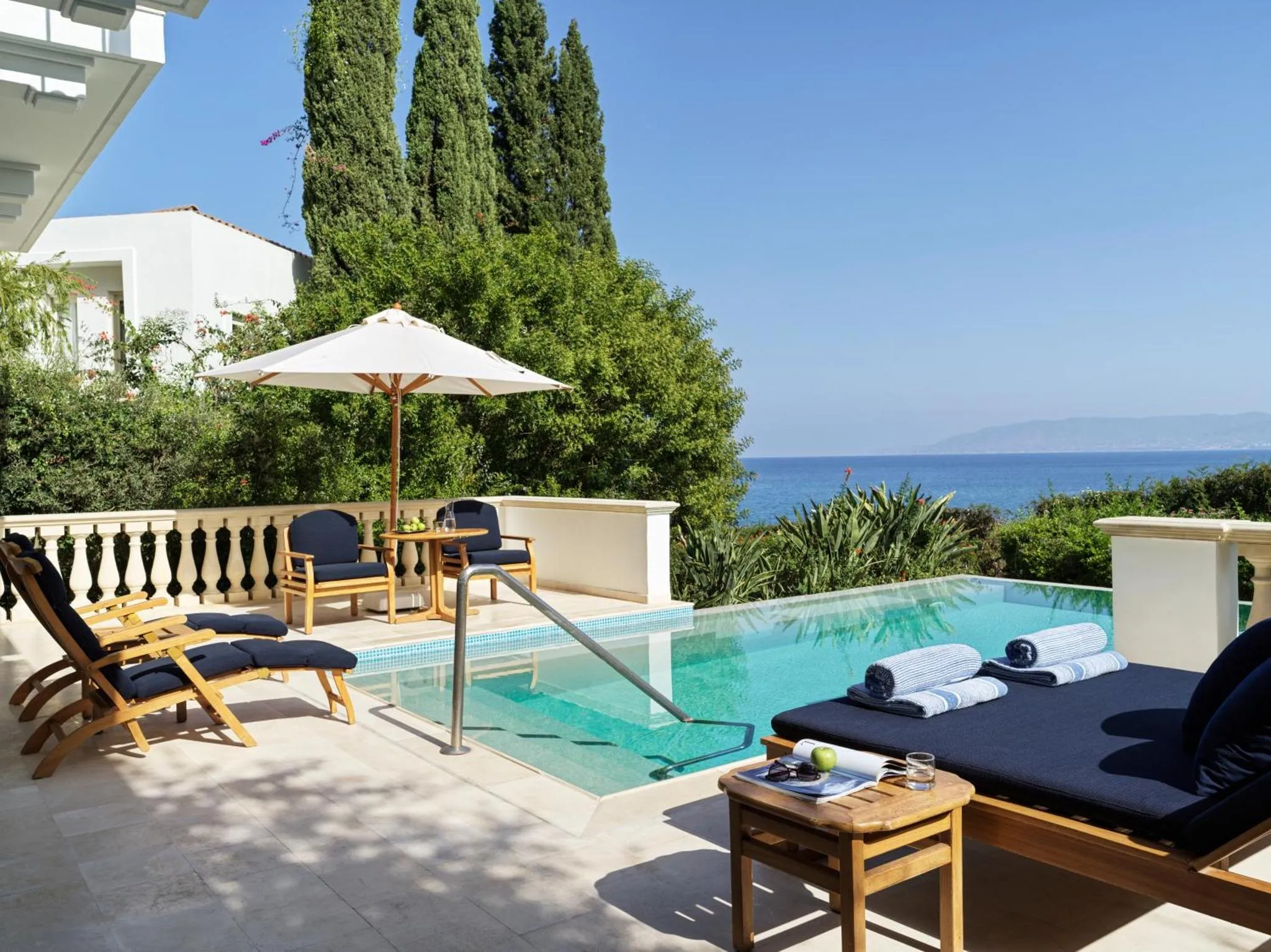 Terrasse avec piscine et chaises longues offrant une vue sur la mer.