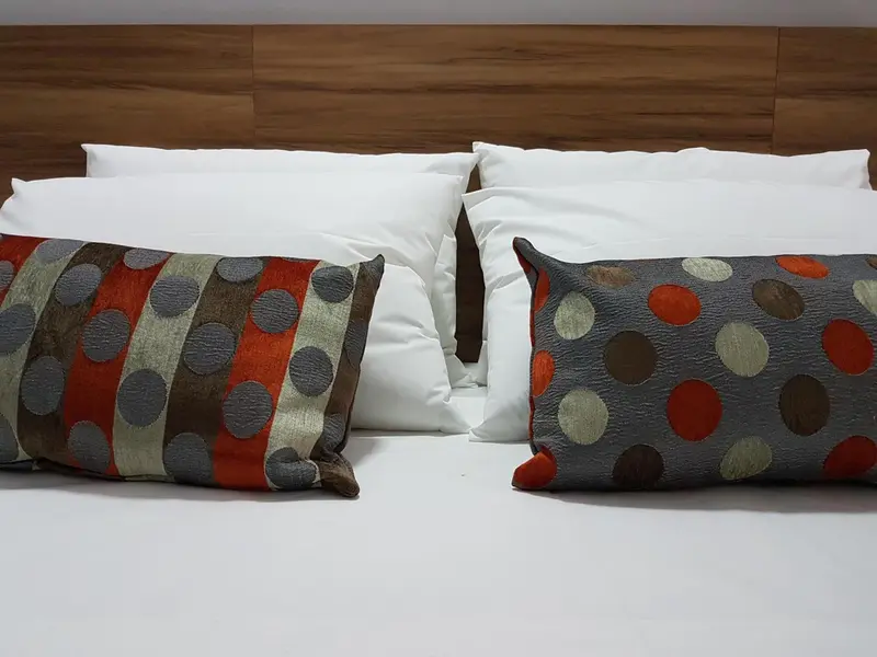 Un lit double est recouvert de draps blancs et de coussins décoratifs.