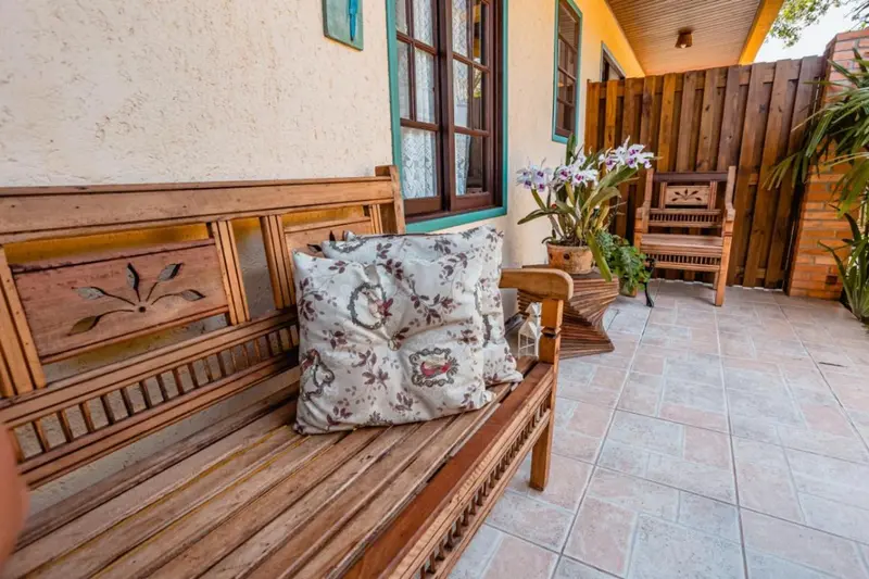 Terrasse avec banc en bois et coussins décoratifs devant une porte fenêtrée.