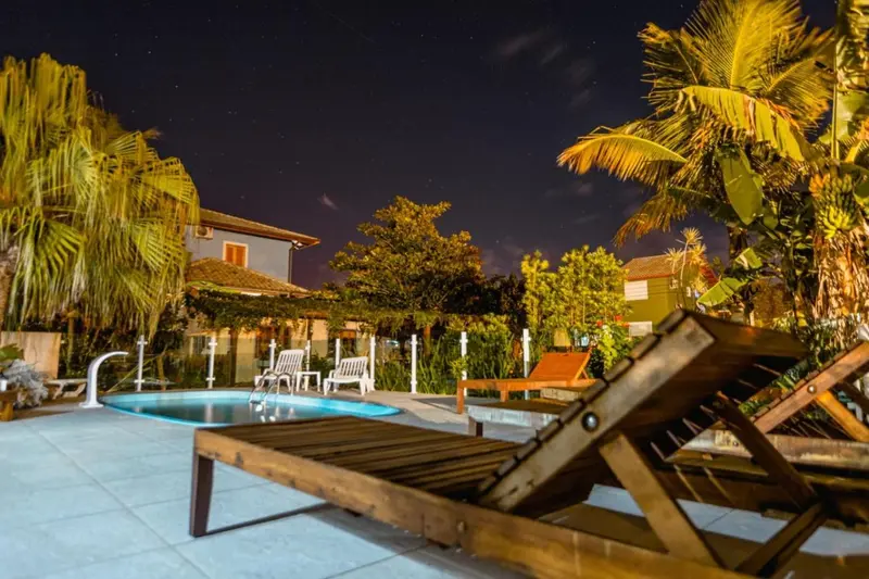 Transats en bois au bord d'une piscine illuminée la nuit.