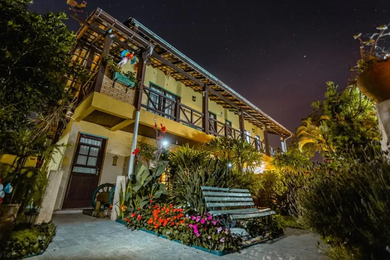 Façade d'un bâtiment jaune éclairé la nuit, avec une terrasse et un jardin fleuri.
