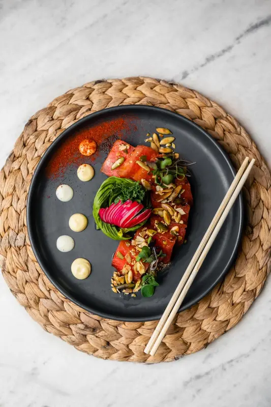 Assiette décorée avec des morceaux de pastèque, des pistaches et des sauces.