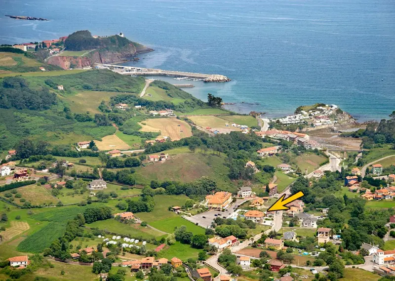 Vue aérienne d'un village côtier verdoyant avec une plage et une presqu'île rocheuse.