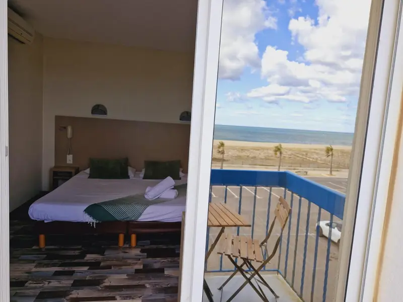 Une chambre lumineuse s'ouvre sur un balcon avec vue sur la mer et la plage.