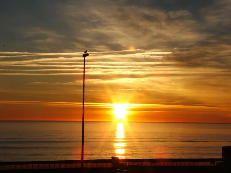 Coucher de soleil sur l'océan avec un mât au premier plan.