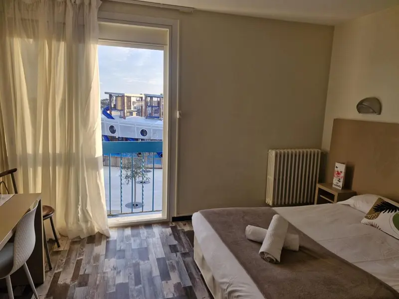 Une chambre lumineuse s'ouvre sur un balcon avec vue sur un port de plaisance.