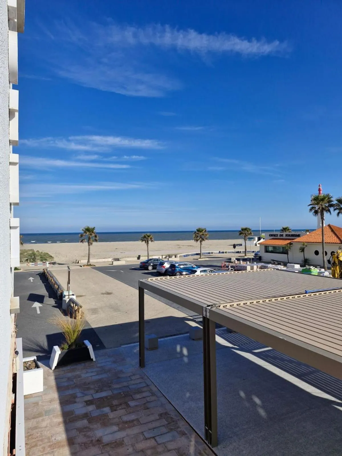 Vue dégagée sur la plage et la mer depuis une terrasse ombragée.
