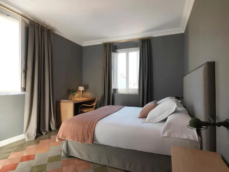 Une chambre lumineuse avec un lit fait et un bureau près de la fenêtre.