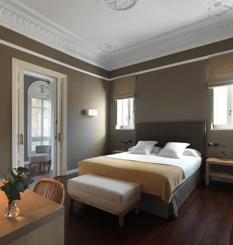 Une chambre lumineuse avec un grand lit et un banc au pied du lit.