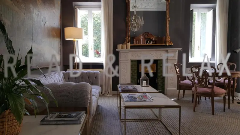 Un salon élégant avec un canapé gris, une cheminée et des fenêtres ouvertes sur un jardin.