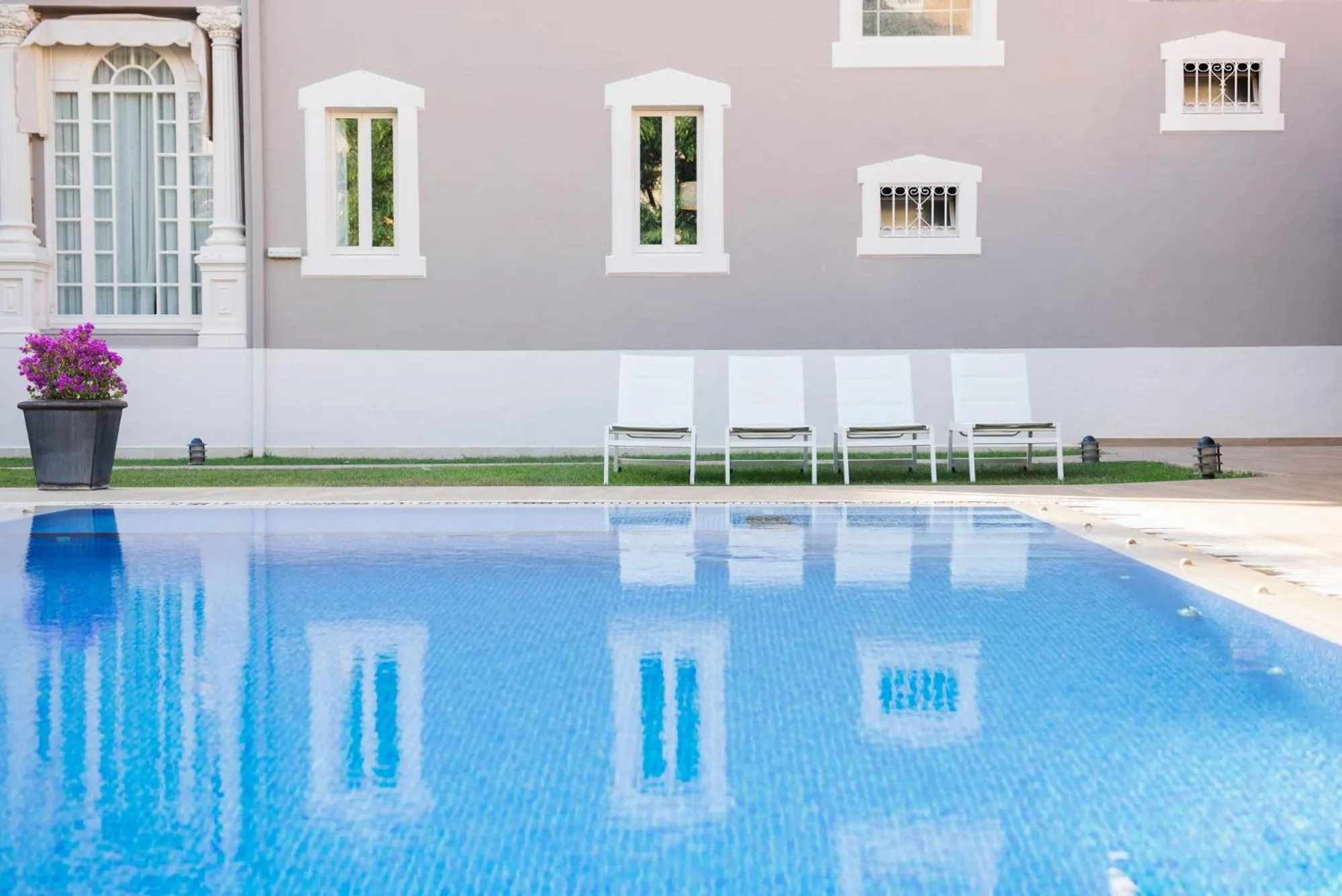 Transats blancs alignés sur une pelouse verdoyante au bord d'une piscine bleue.