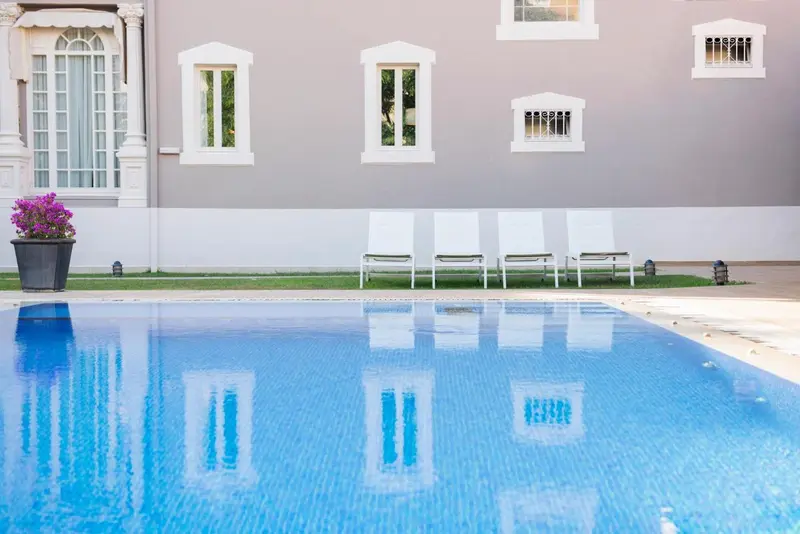 Transats blancs alignés sur une pelouse verdoyante au bord d'une piscine bleue.