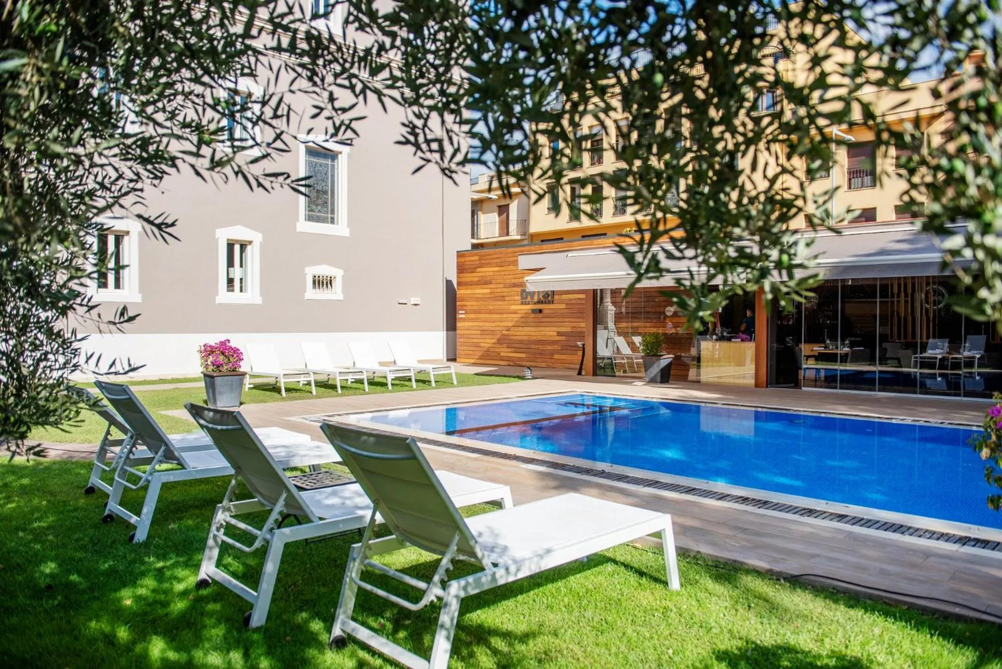 Transats blancs disposés autour d'une piscine rectangulaire dans un jardin verdoyant.