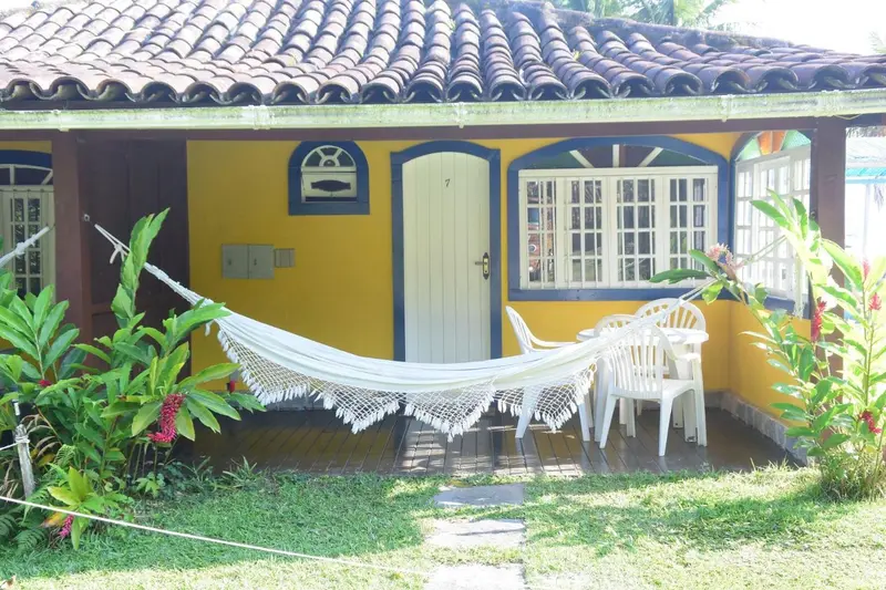 Une maison jaune avec un hamac suspendu devant la porte.