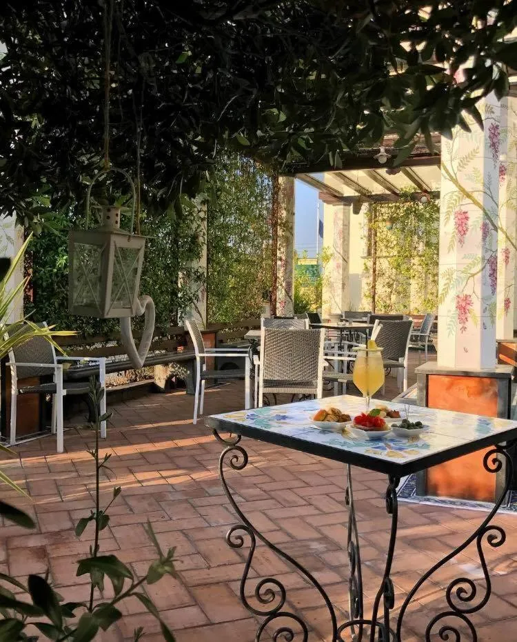 Une table est dressée sur une terrasse ombragée avec des chaises et des plantes.